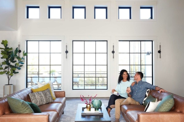 Coupling chatting on sofa in living room with large Pella Impervia windows