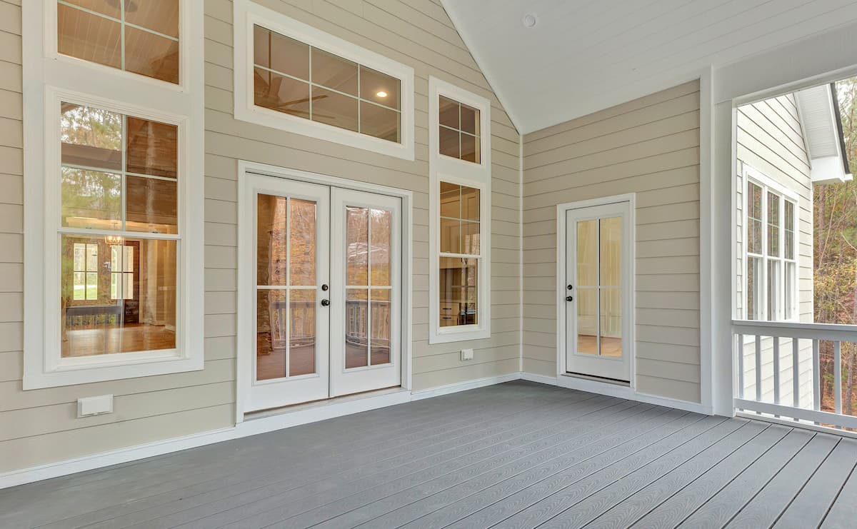 View from a covered patio onto a home with white double-hung windows and patio doors