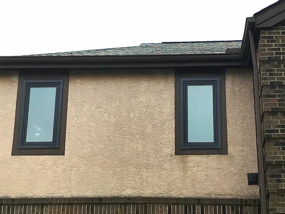 Exterior view of two new brown vinyl casement windows on a Tudor-style home