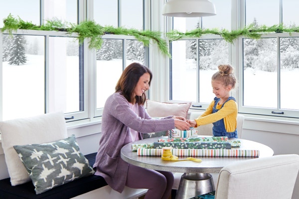 mom and daughter wrap presents comfortably in a room full of windows