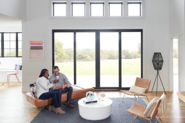 Couple talks in living room with black multi-slide patio doors with fixed windows above