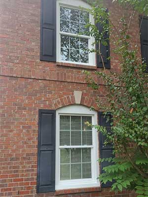 Post-installation shot of white vinyl windows with black shutters on brick Brentwood, TN, home