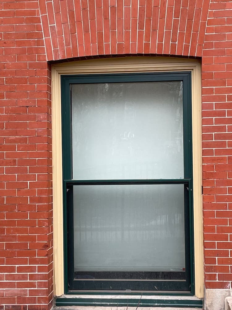 Close up of black replacement window with wood frame on the red brick building's exterior.
