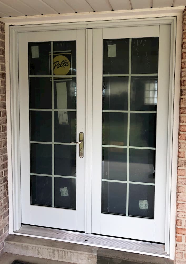 Exterior view white hinged French patio door with traditional grille pattern on brick home