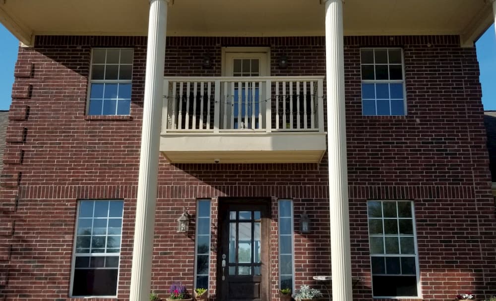 Exterior view of front of two-story red brick home with old aluminum double-hung windows