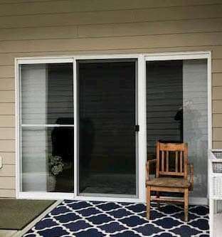 Exterior view of old sliding patio door on a home with tan siding