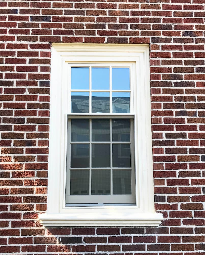 Exterior view of white wood double-hung window on red brick home