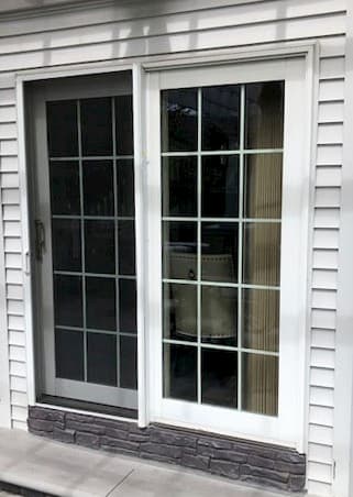 Exterior view of old white sliding patio door with traditional grille pattern