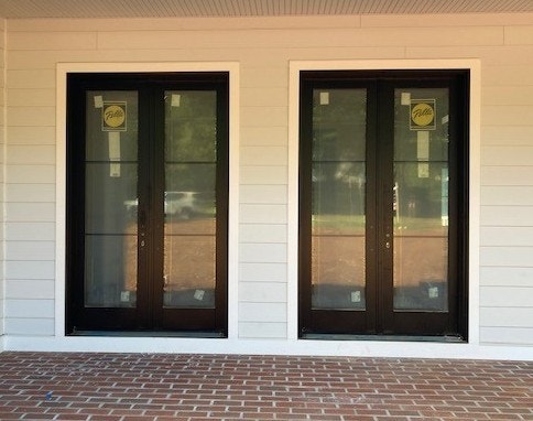 Exterior view of two sets of black French doors on a home with white siding