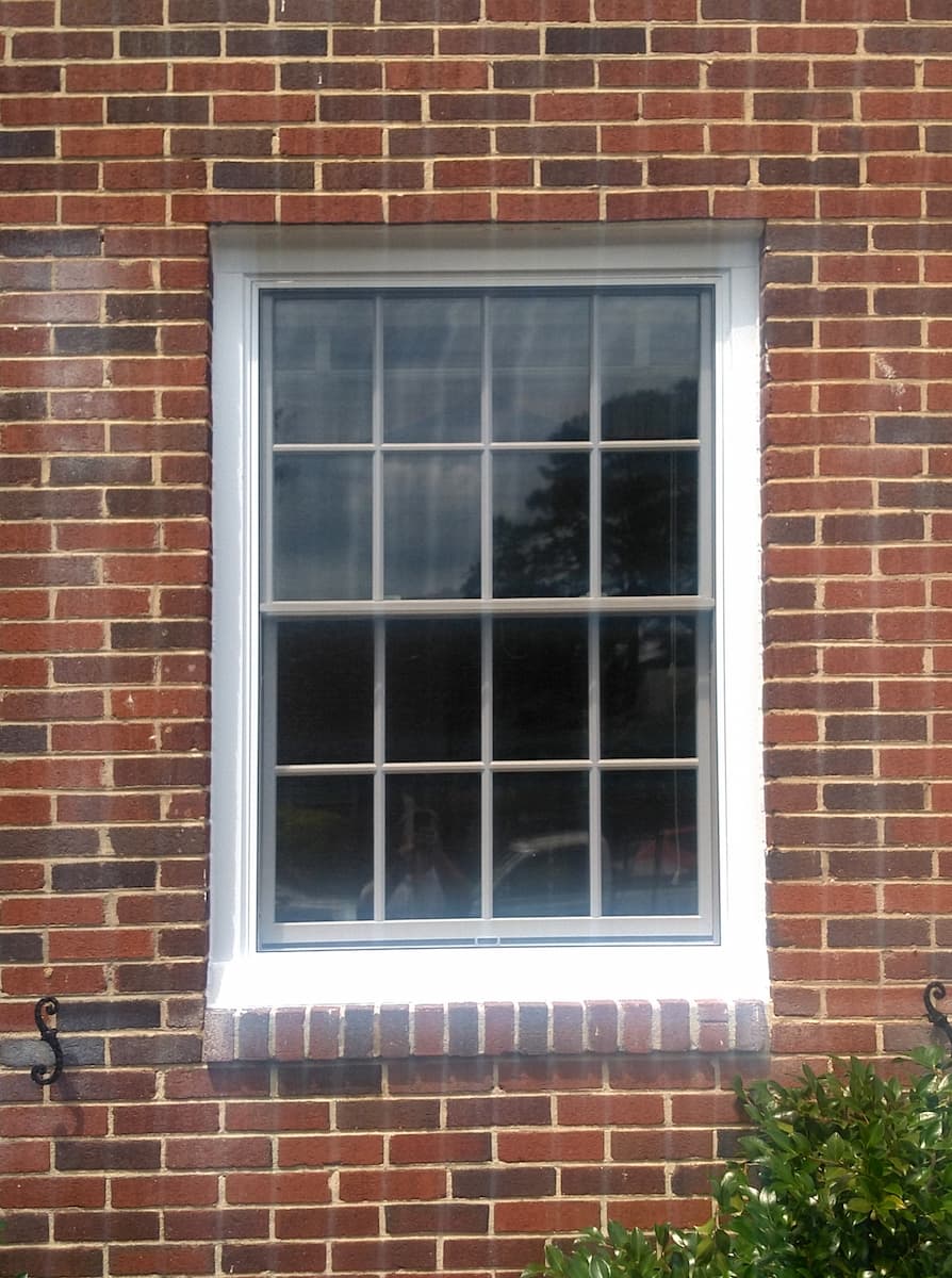 Exterior view of white wood window with traditional grilles on a red brick home