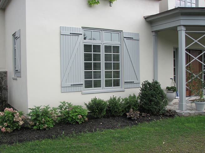 Gray wood casement windows with traditional grille profiles and gray decorative shutters