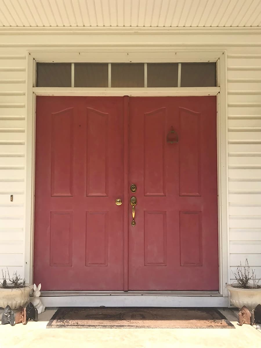 Old red double entry doors on a white home