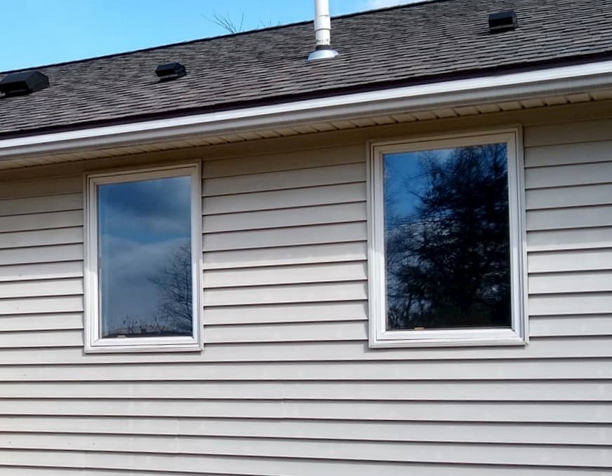 Exterior view of two white fixed windows on a home with beige siding