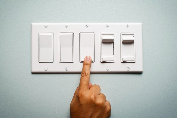 a row of light switches with a hand turning the middle switch off