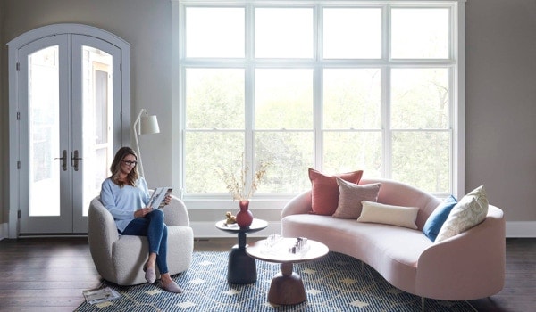 Woman reading in chair in front of white floor-to-ceiling windows