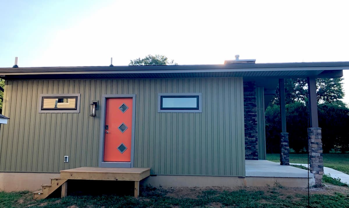 Side view of new green home with orange door and fiberglass windows
