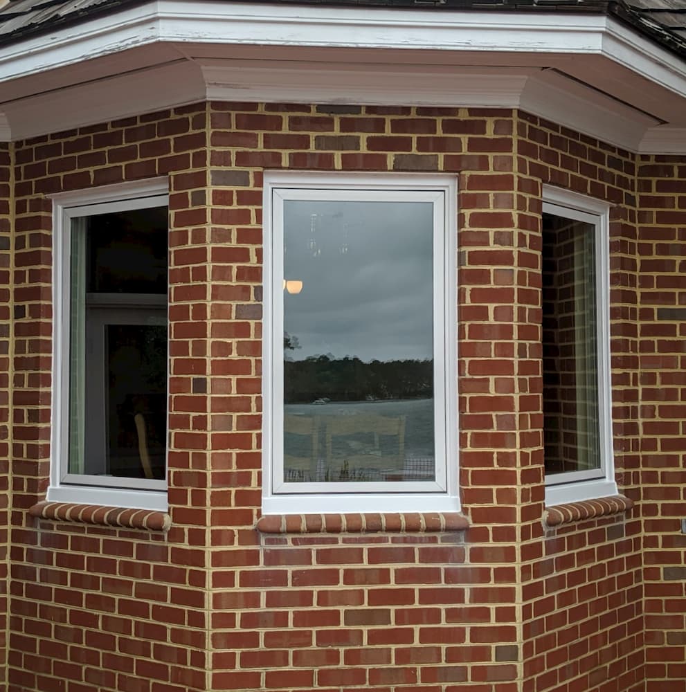 Exterior view of new white fiberglass casement windows on red brick home