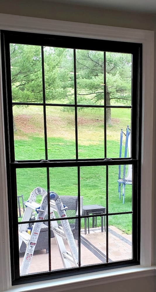 New large fiberglass double-hung window with traditional grille pattern and black finish