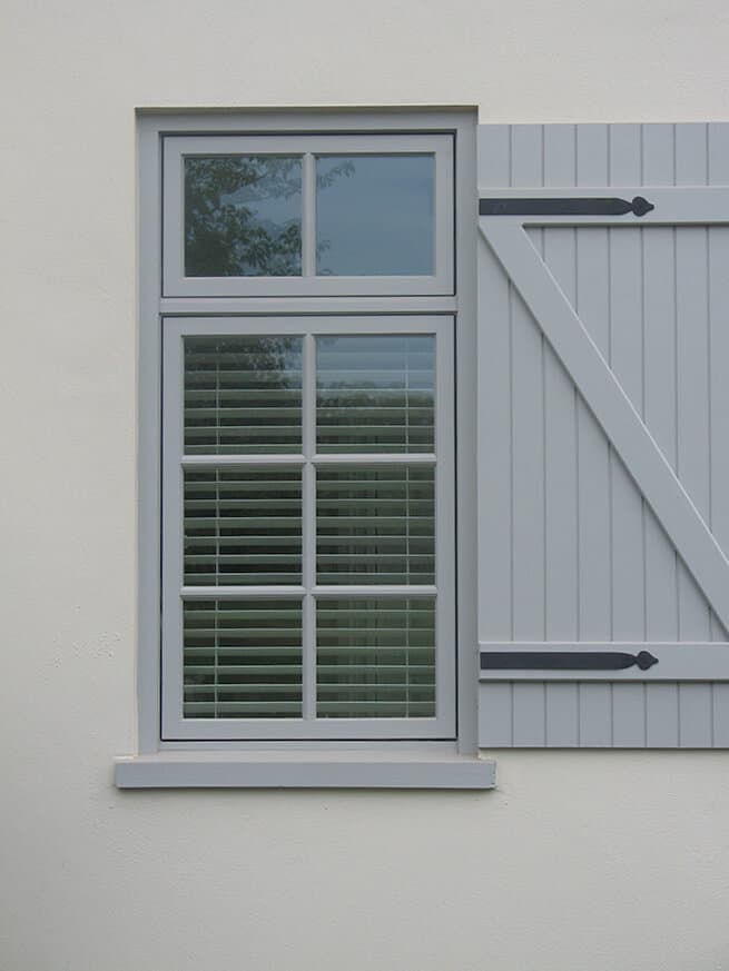 Gray wood casement window with traditional grille pattern and transom window