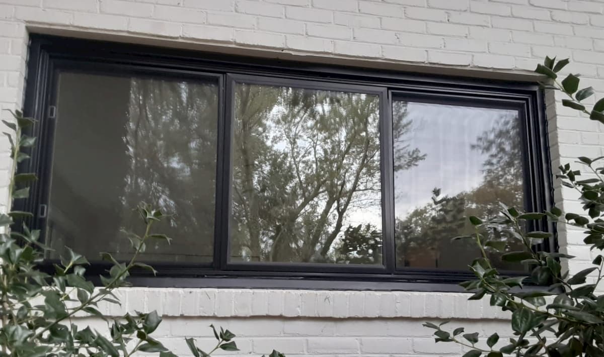 exterior view of black sliding fiberglass window on gray painted brick home