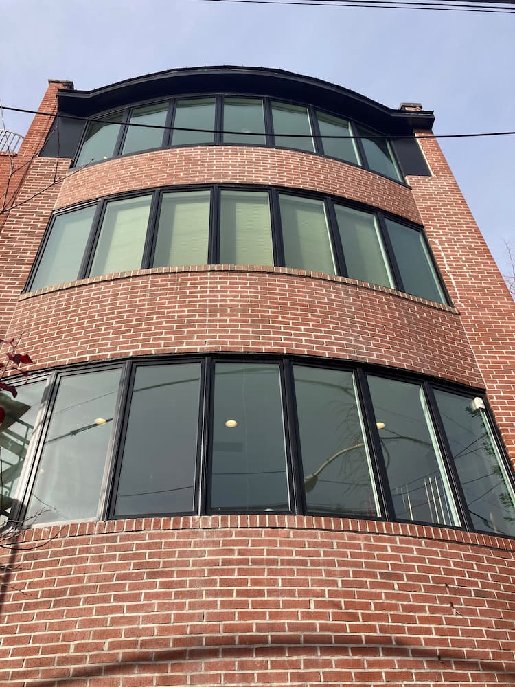 Street view and upward angle of towering brick building featuring seven black custom bow windows
