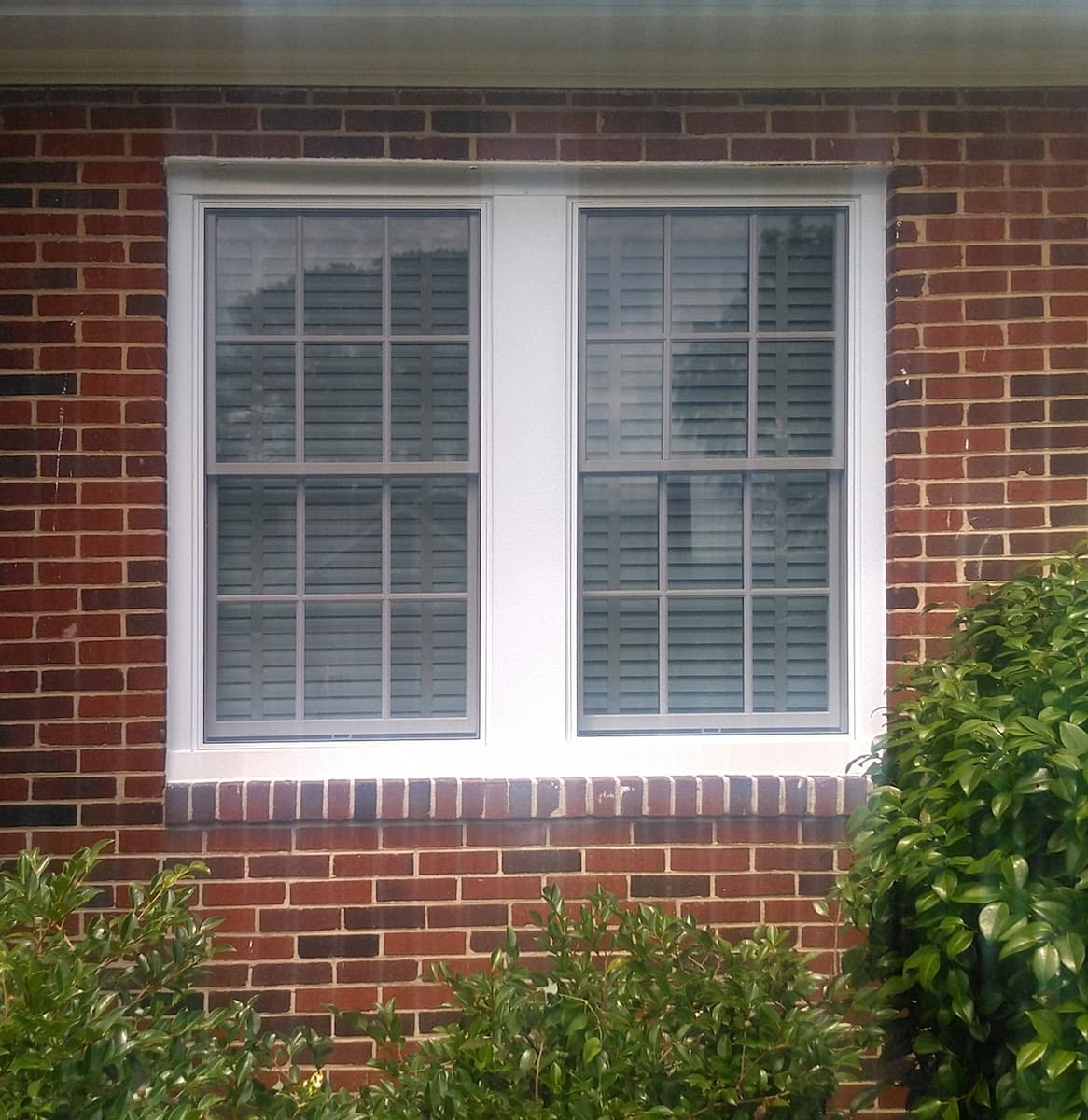 Exterior view of white wood windows with traditional grilles on a red brick home