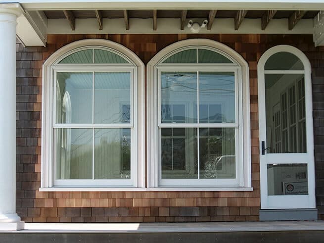 Two wood double-hung windows with special shape transoms on a shingle-style home