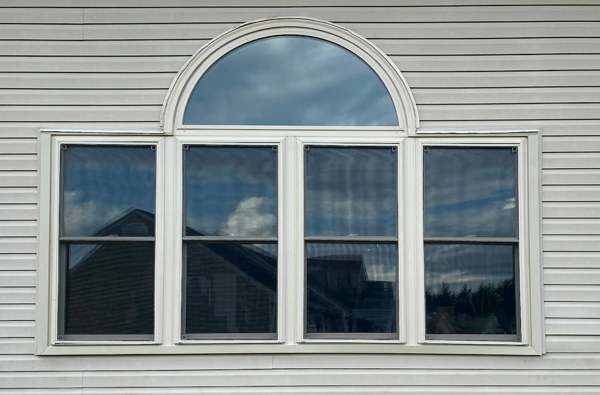 Exterior view of four vinyl double-hung windows with a half-arch transom.