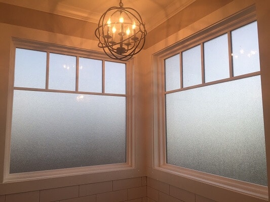 Interior view of two frosted bathroom windows with white grilles inside a new-build, farmhouse-style