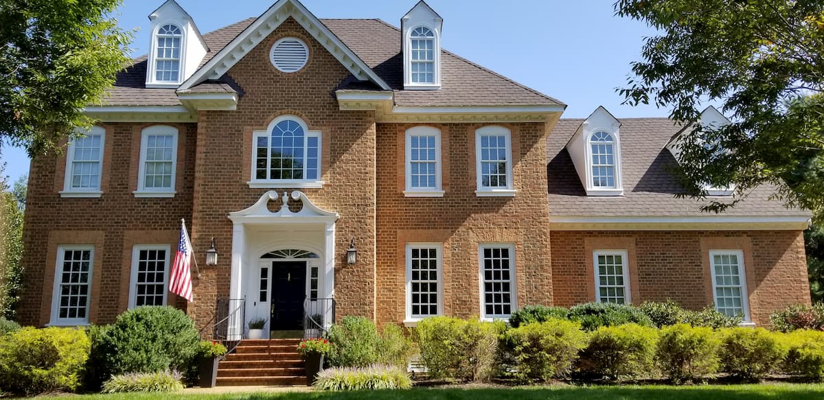 Front exterior view of stately two-story brick home with white wood double-hung windows