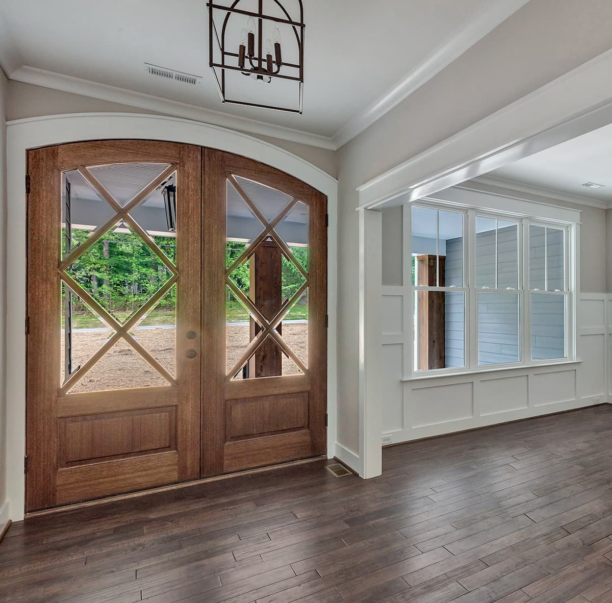 Foyer with view to double wood entry doors and three white double-hung vinyl windows