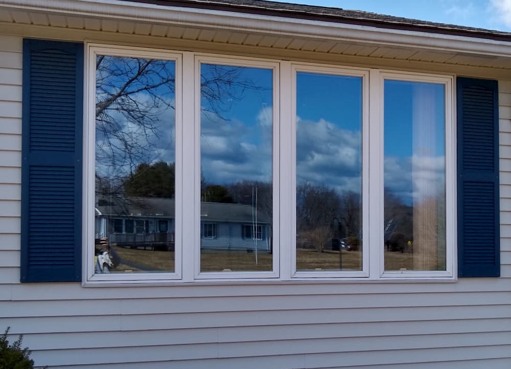 Exterior view of four side-by-side casement windows between green shutters 