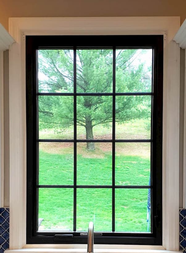 Black double-hung fiberglass window with traditional grille pattern above kitchen sink