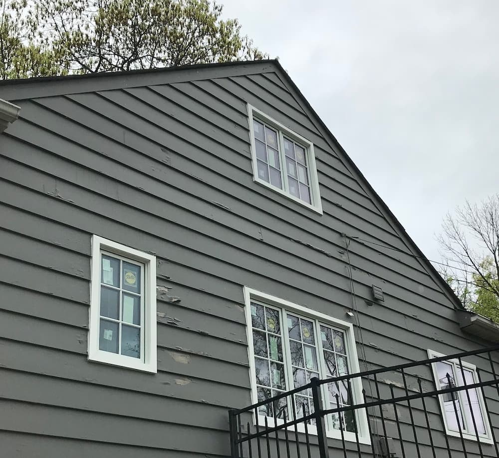 Exterior view of the side of a gray Cape Cod-style home with all-new wood casement windows