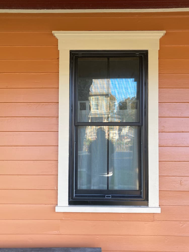 Close up of orange home featuring new black wood windows with grilles