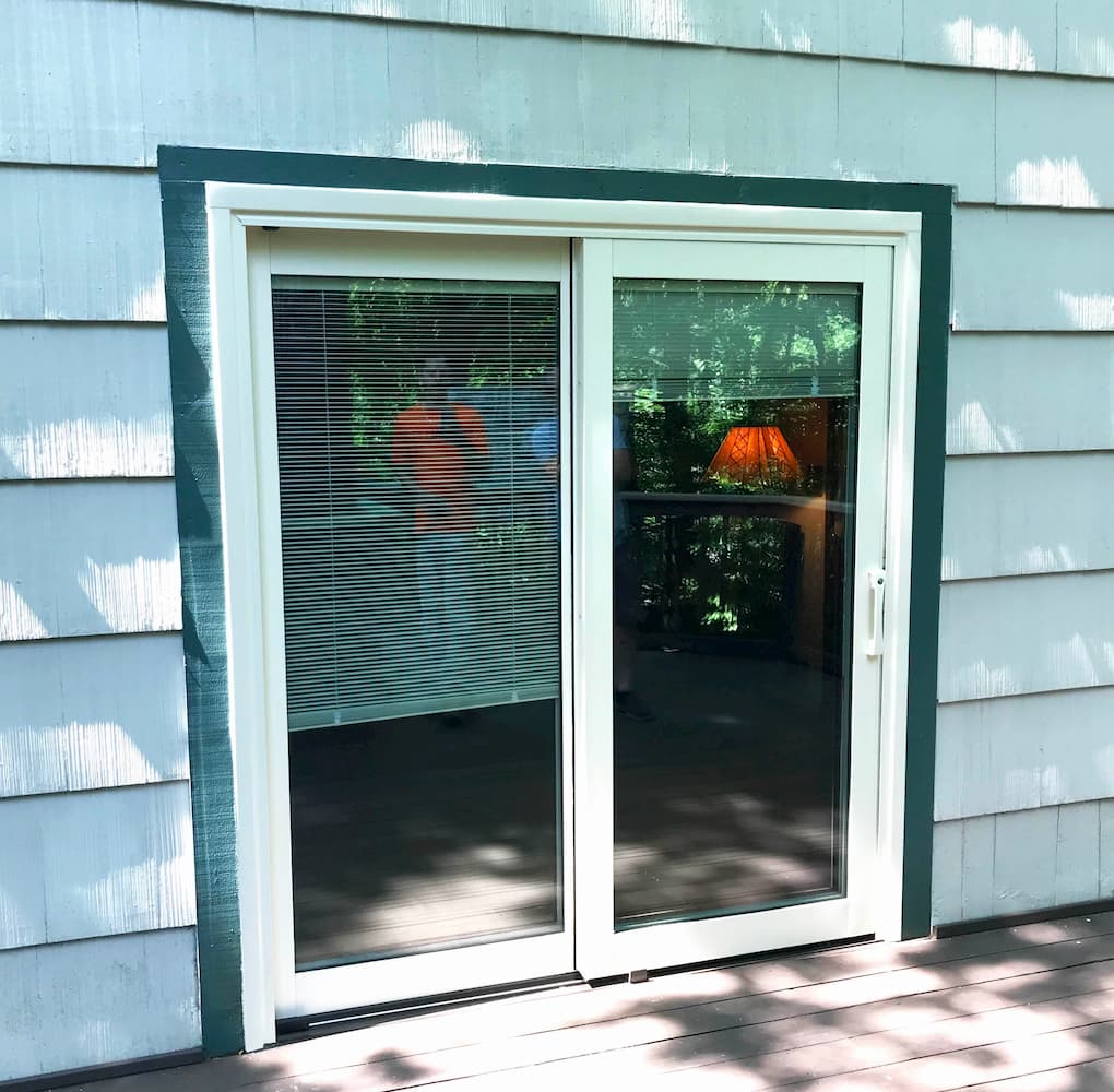 Exterior view of new white sliding patio door on a home with white shingles