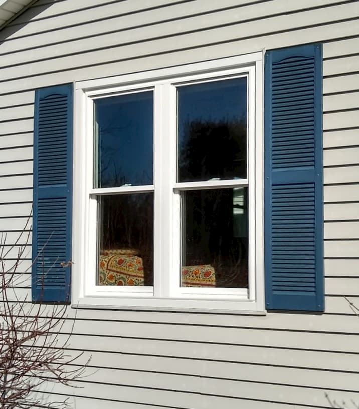Exterior view of two white vinyl double-hung windows between blue shutters on beige home.