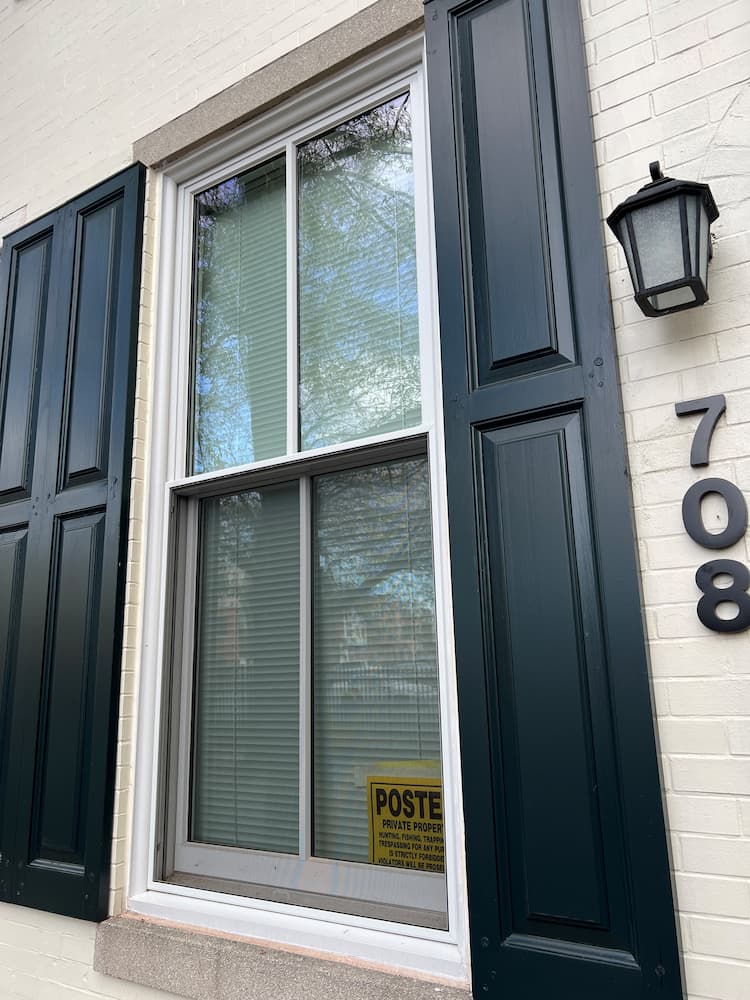 Close-up of white double-hung windows with black shutters on white brick historic townhomes