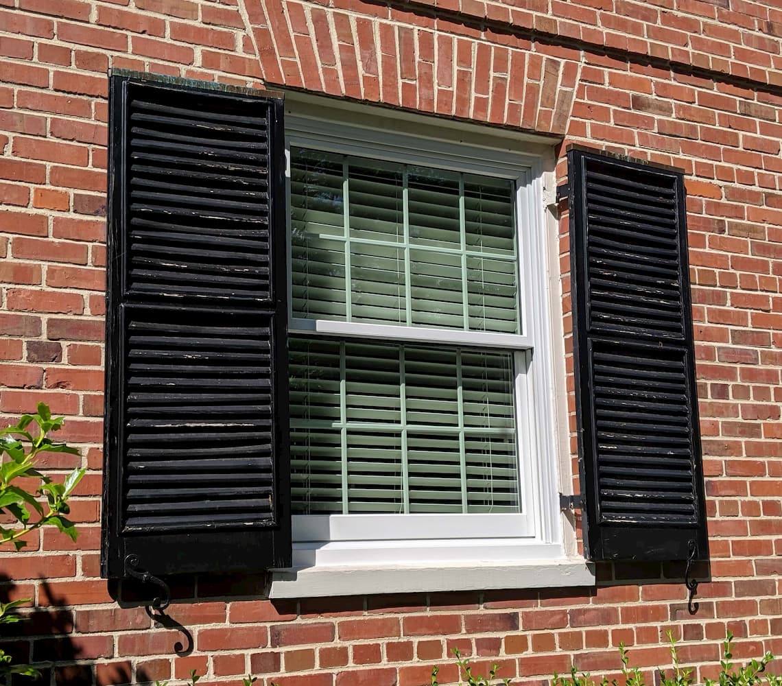 Red brick home with new white wood window and black shutters