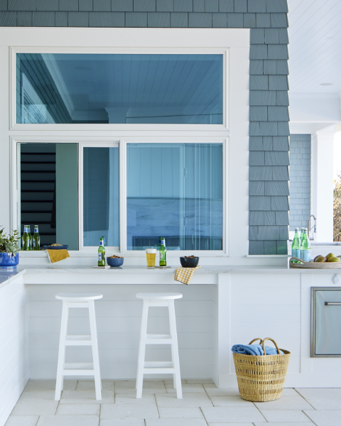 An outdoor kitchen bar attached to the house with a Pella sliding window for easy entertaining