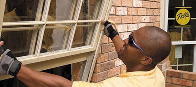 Man replacing double-hung window on a brick home