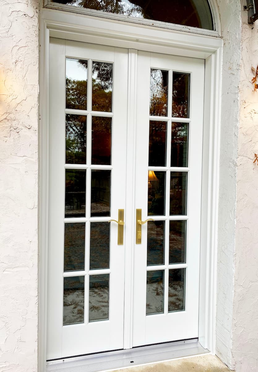 Exterior view of new white wood French door with brass handles.