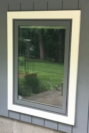 Close-up exterior view of new gray casement window with white trim on a gray home