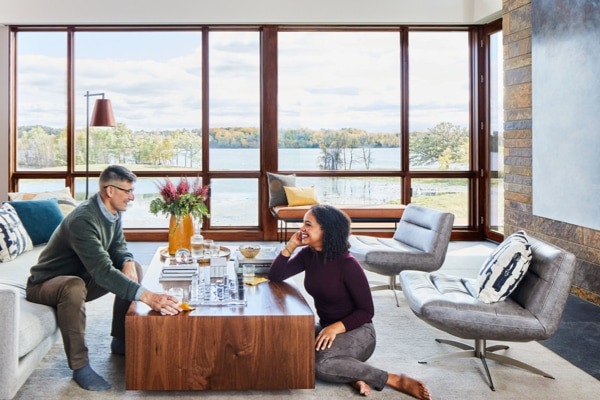 Family talking in front of wall of glass made with large, wood picture windows overlooking lake view