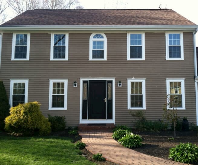 Front exterior view of two-story beige home with white vinyl windows and new black entry door