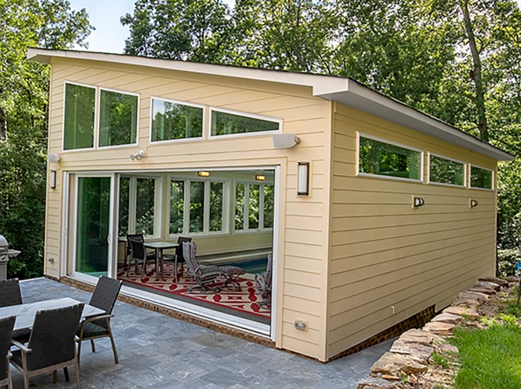 Exterior view of pool house with white vinyl windows and open sliding patio door