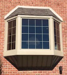 Exterior view of new wood bay window with traditional grille pattern on a red brick home
