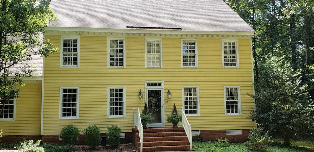 Exterior view of two-story yellow home with old vinyl double-hung windows on the first floor
