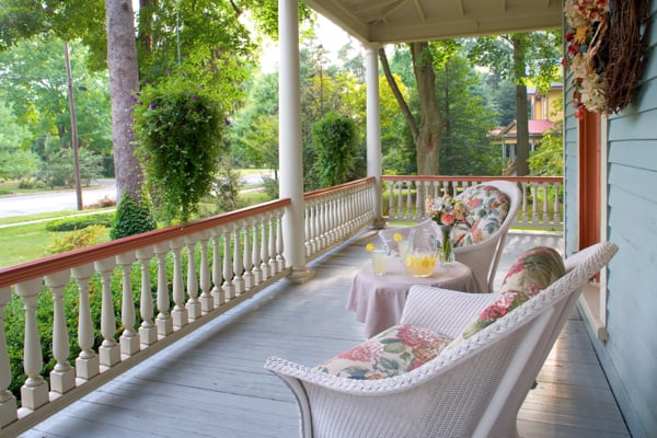 An expansive wraparound porch on a Victorian Style house with charming white wicker seating