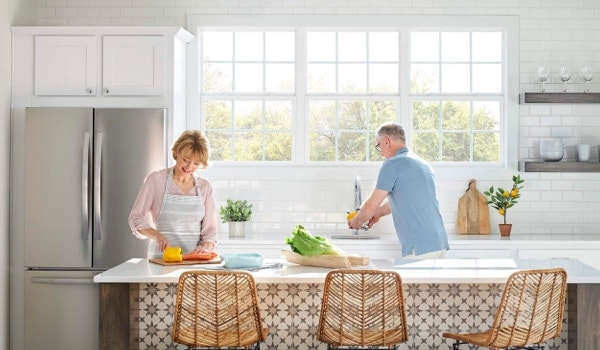 Couple preparing meal in kitchen with windows and indoor plants
